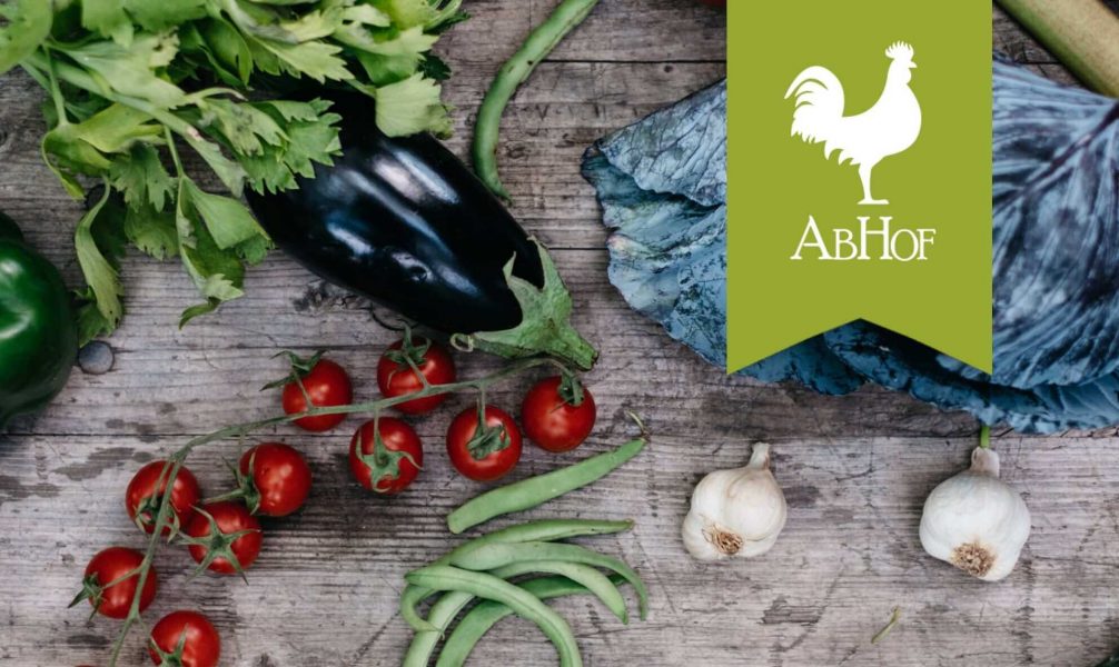 The brand Abhof which is represented by a white rooster on green background with vegetables on a wooden table in the background